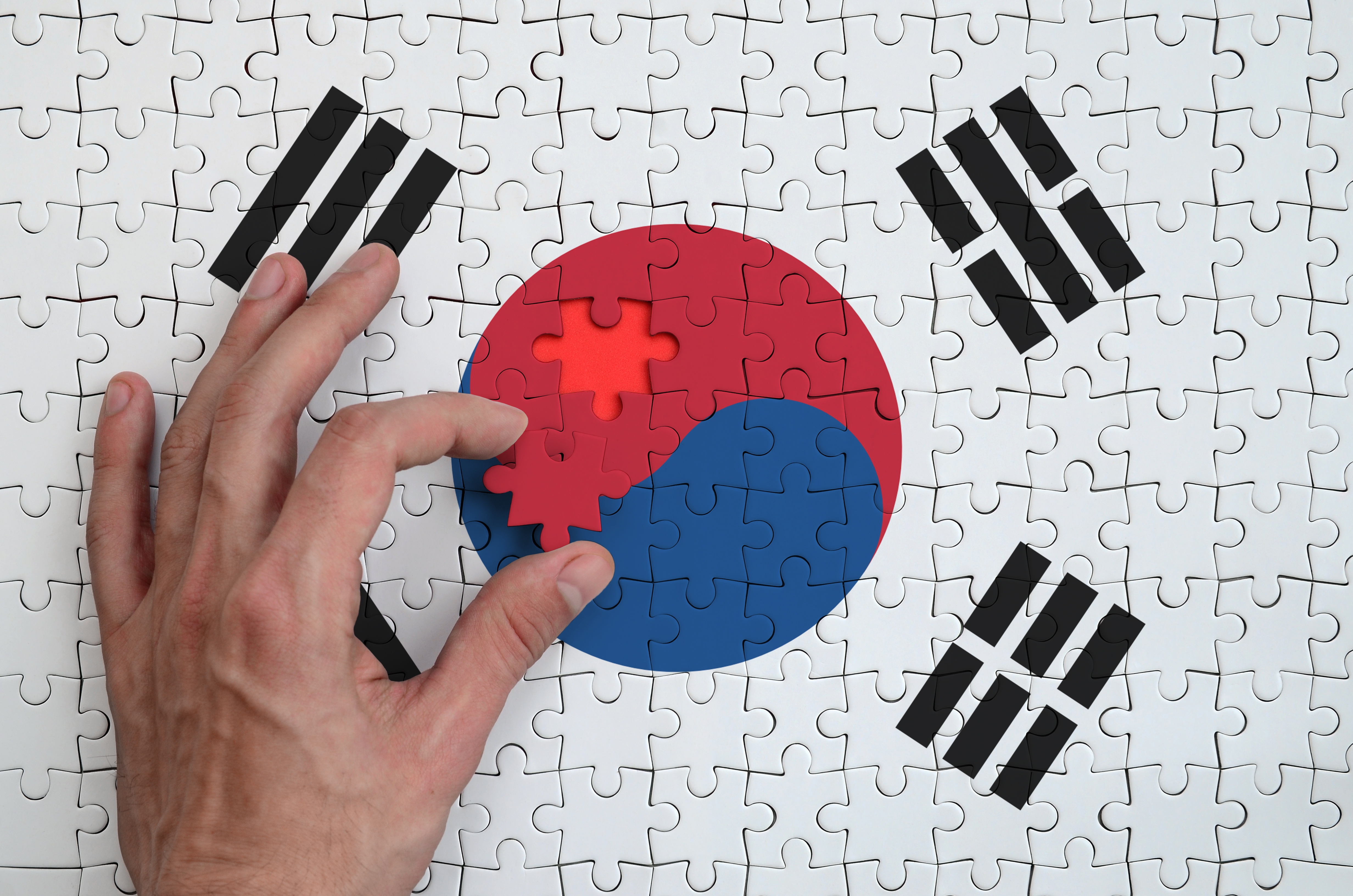 South Korea flag is depicted on a puzzle, which the man's hand completes to fold.