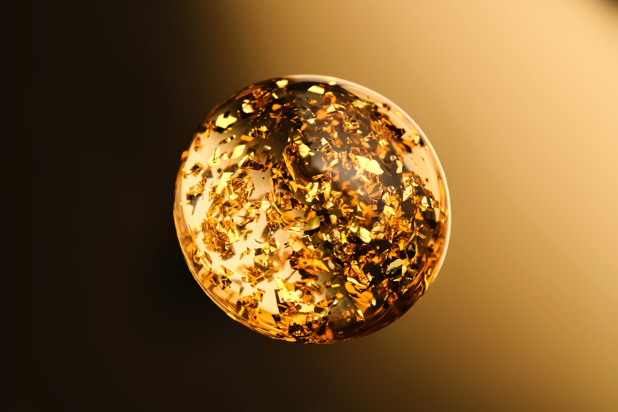 A round drop of 24k gold serum on a gold background.